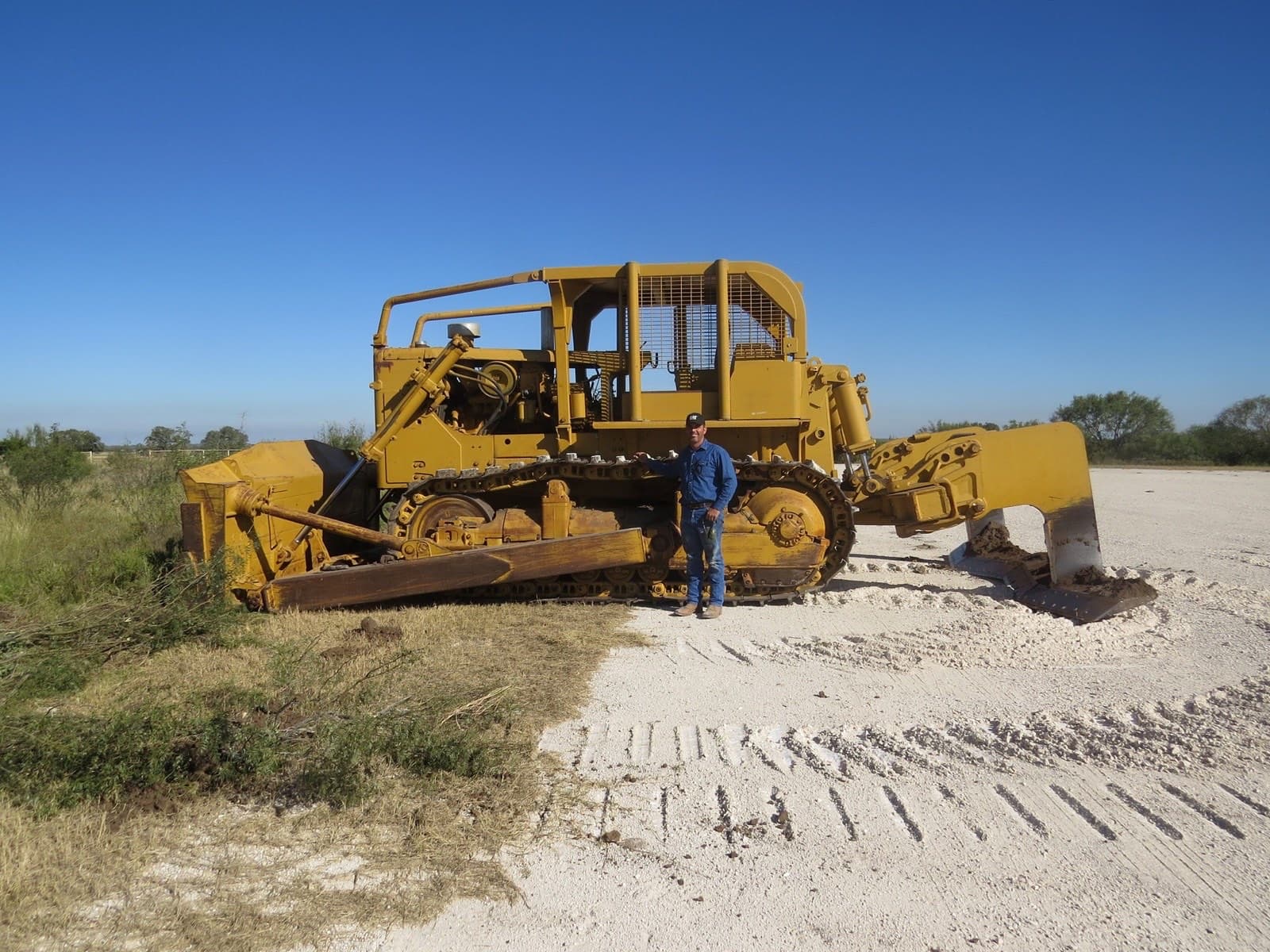 Joe Neal standing beside the 1969 Caterpillar D9G dozer with 16ft root plow in South Texas